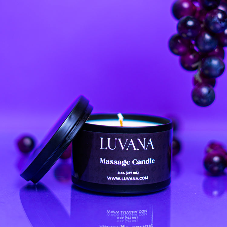 Lit Luvana Massage Candle with lid beside it on purple background with grapes, soy wax massage oil candle made in Puerto Rico.