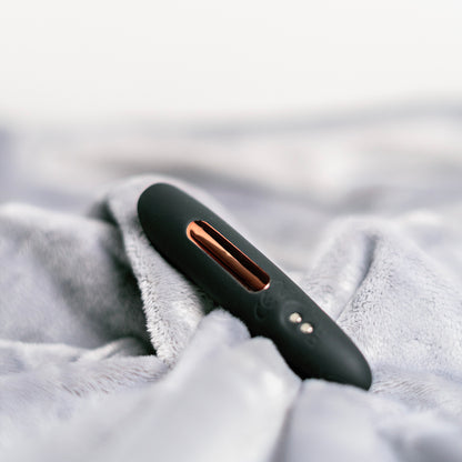 Close-up of Luvana Mini Bliss bullet vibrator resting on soft plush fabric, matte black with rose-gold accent.